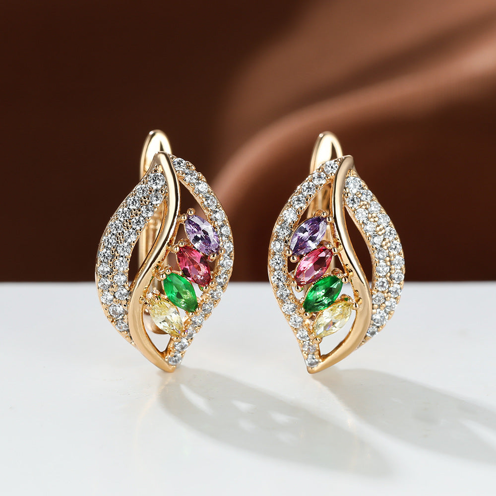 Gold earrings with colorful gemstones on a white surface with a brown background
